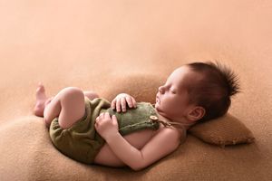 Sleeping newborn baby in fetal position on soft peach-colored backdrop.