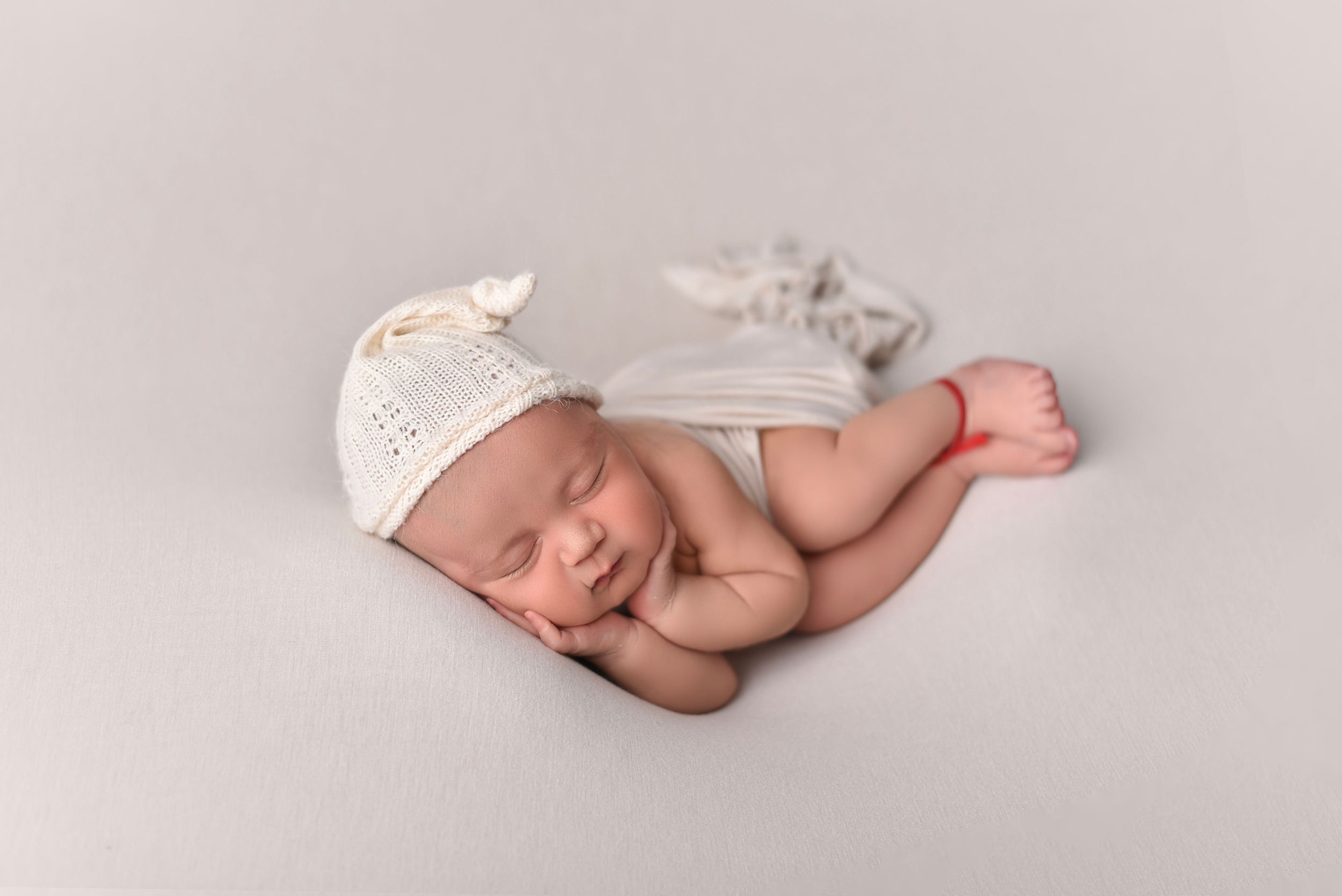 Sleeping newborn in white lace wrap positioned artistically on light grey background.