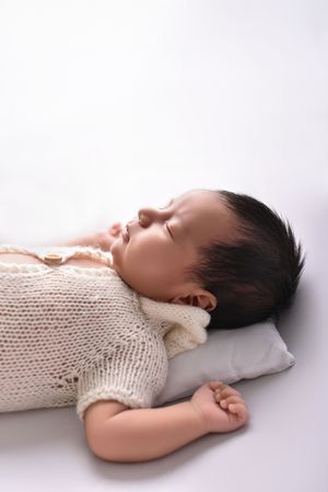 A baby in a white knit sweater lies peacefully on a white pillow in a series of resting poses.