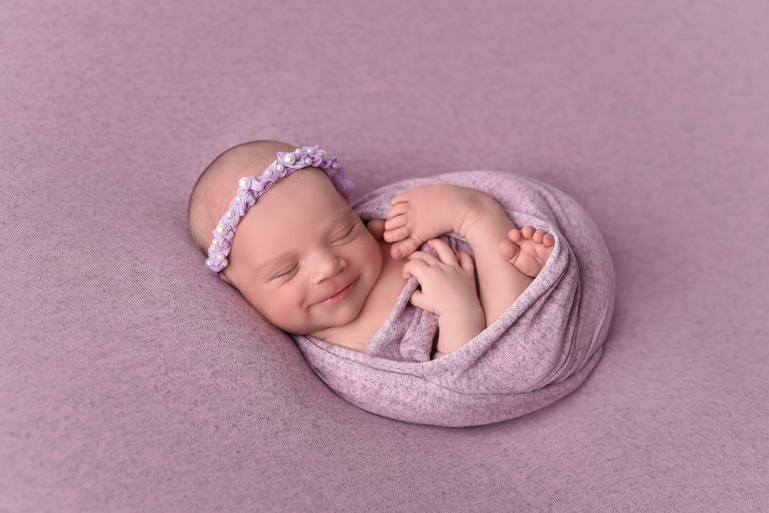 Sleeping newborn wrapped in purple swaddle with matching headband.