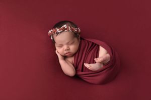 Peaceful newborn photography session on deep burgundy backdrop with gentle wrapping.