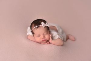 Sleeping newborn wearing delicate white headband on pink background.
