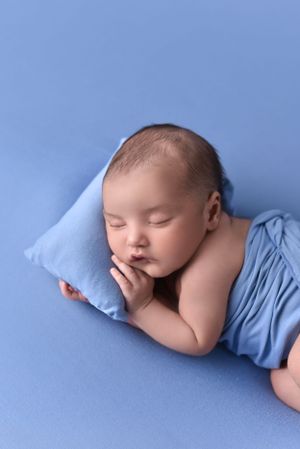 Sleeping newborn in light blue wrap resting head on matching pillow.