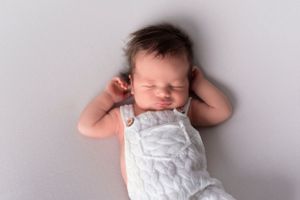 Sleeping newborn in white outfit lying on grey backdrop during professional photo session.