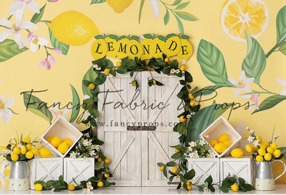 A rustic lemonade stand setup with white wooden doors, floral garland, and yellow lemons against a yellow patterned backdrop.