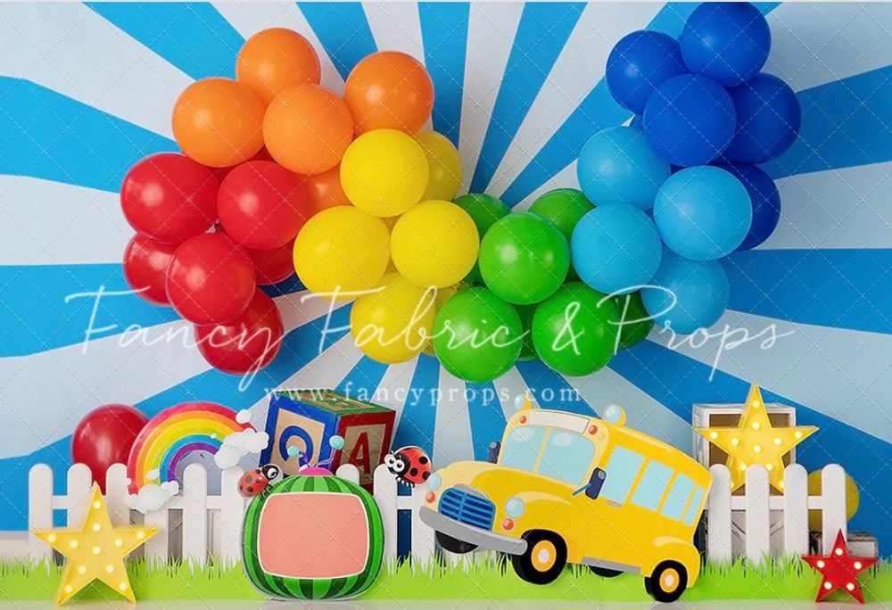 Rainbow balloon arch with school bus and picket fence decorations against blue sunburst background.