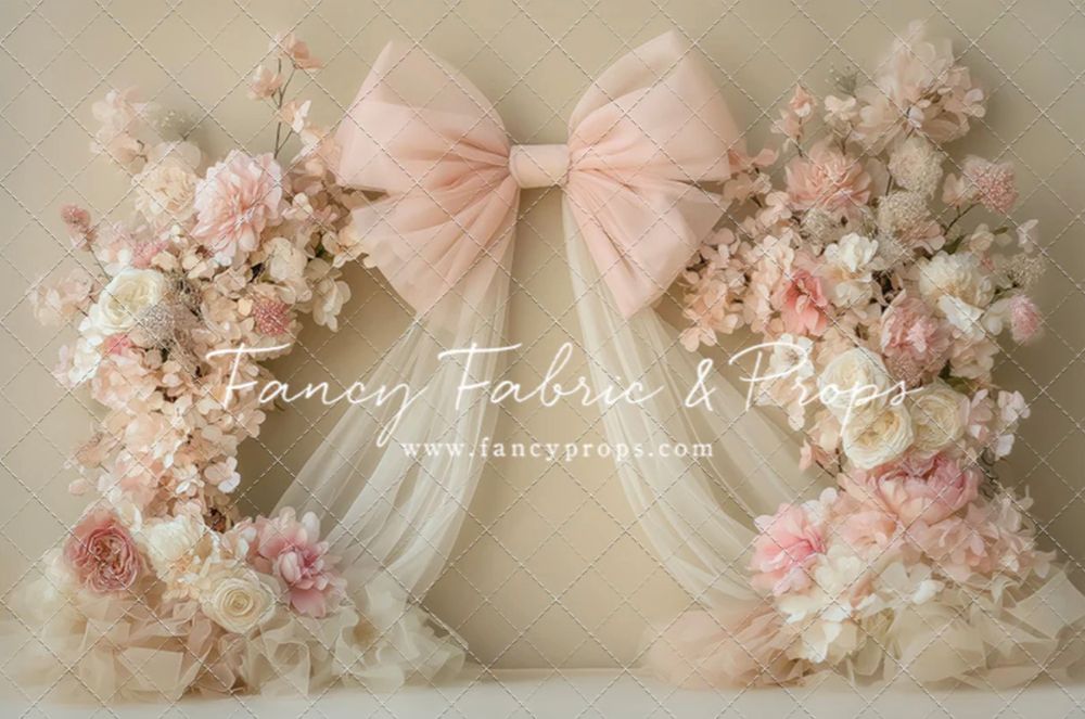 Soft pink and white floral arch backdrop with delicate roses and a large blush bow centerpiece for photography.