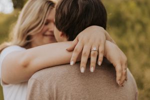 A romantic embrace in golden sunlight with an engagement ring visible.