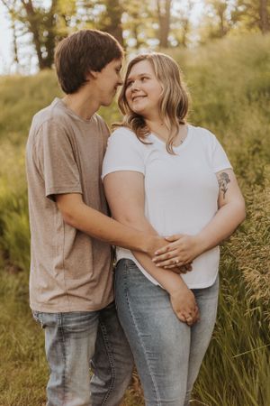 Sweet candid moment between couple standing in tall grass during golden hour.