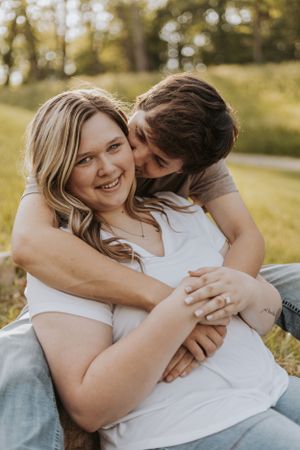 A tender embrace between a couple outdoors with natural sunlight filtering through trees in the background.