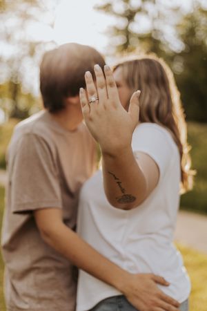 An engagement ring is showcased as a couple shares a kiss in warm sunlight.