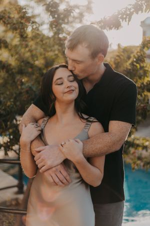 A romantic couple embraces near a pool during golden hour.
