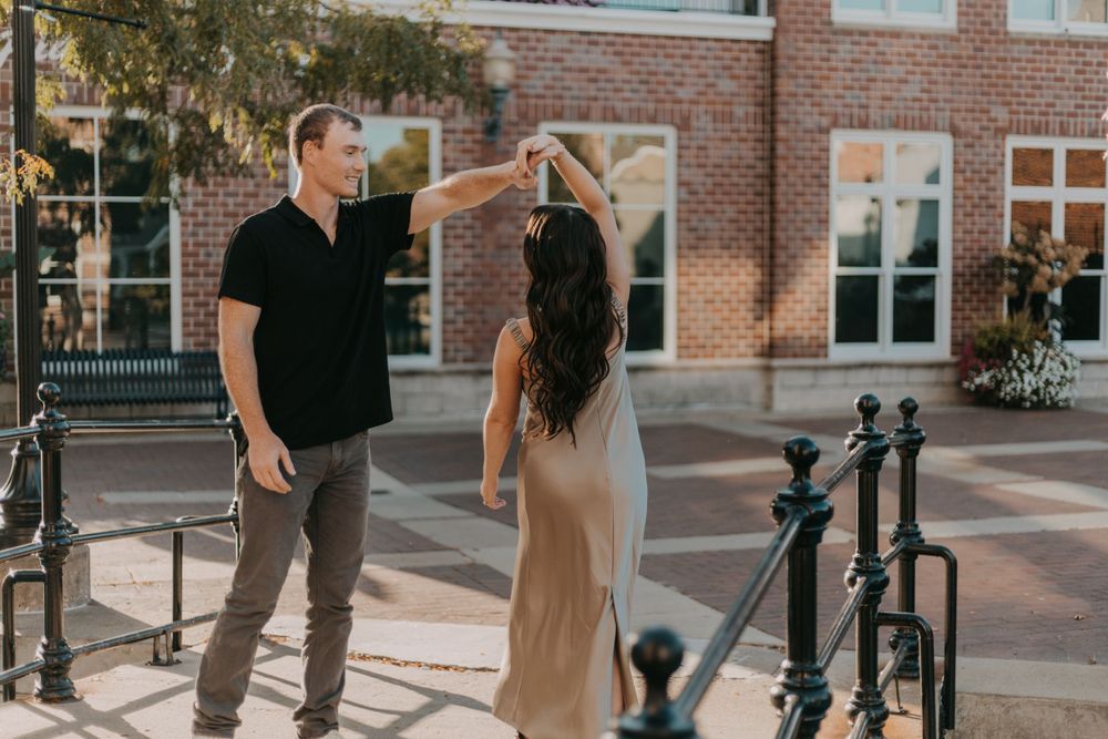 A couple sharing a playful moment on an urban walkway with brick buildings behind them.