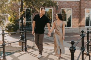 A couple holding hands while walking along a brick building exterior during daytime.