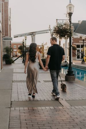 A couple walks hand in hand down a charming brick-paved street at sunset with vintage lampposts.