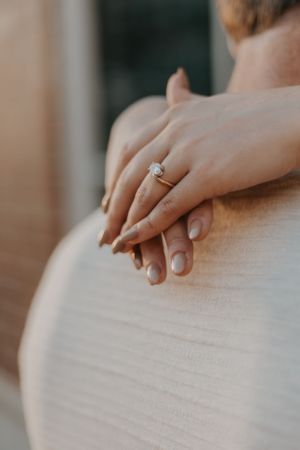 Close-up shot of hands with an engagement ring resting on a white surface in soft natural light.