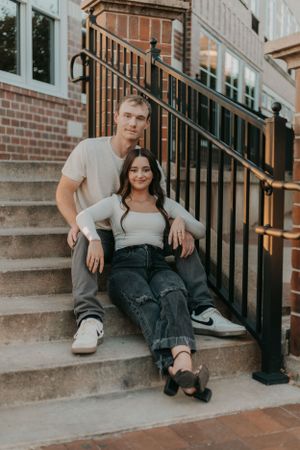 Couple sitting casually on concrete steps with brick building backdrop.