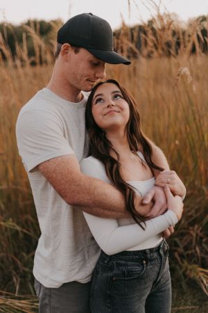 Loving couple embracing in golden field during sunset photo session.