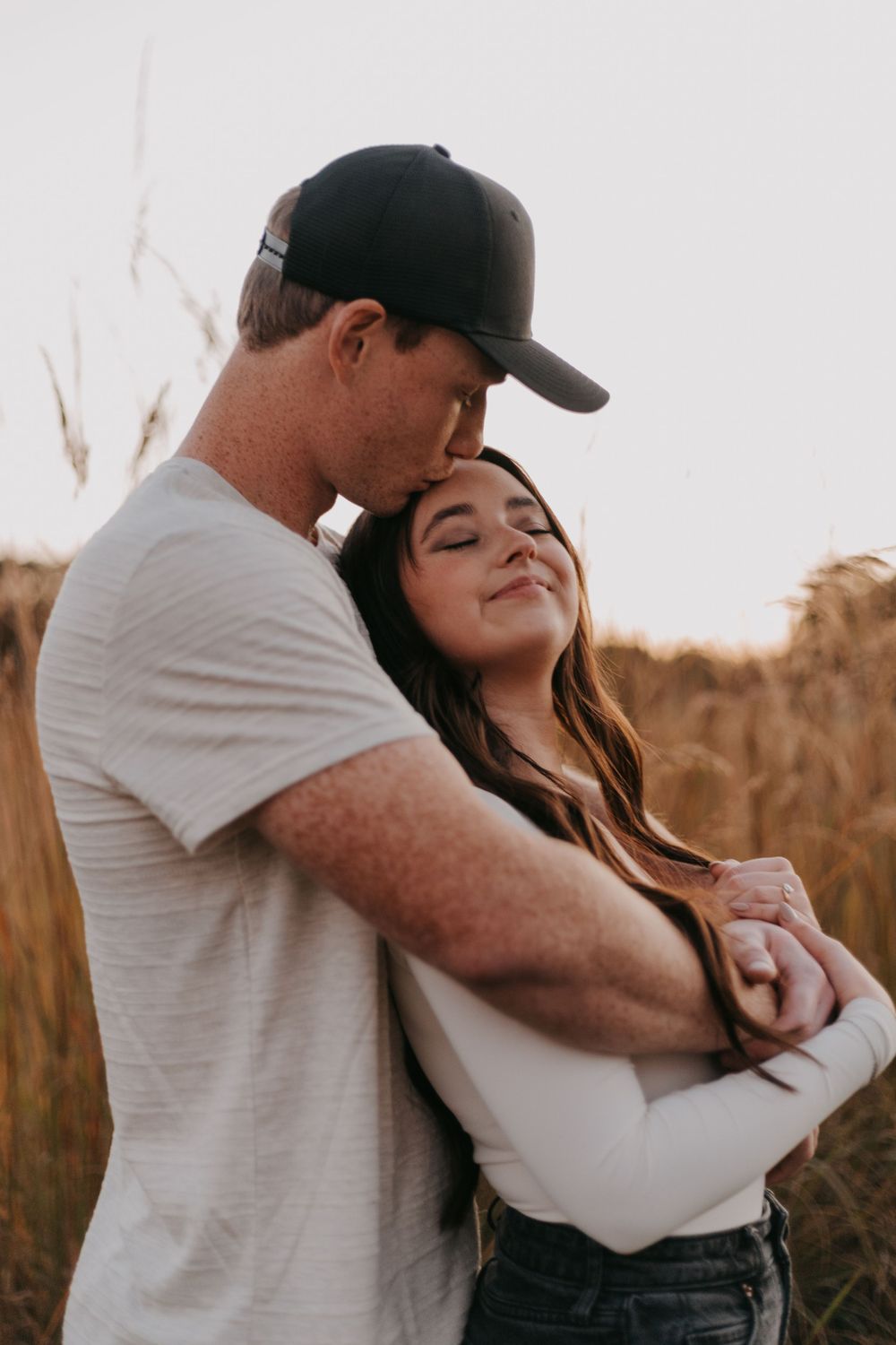 Tender moment between couple embracing in field at sunset.