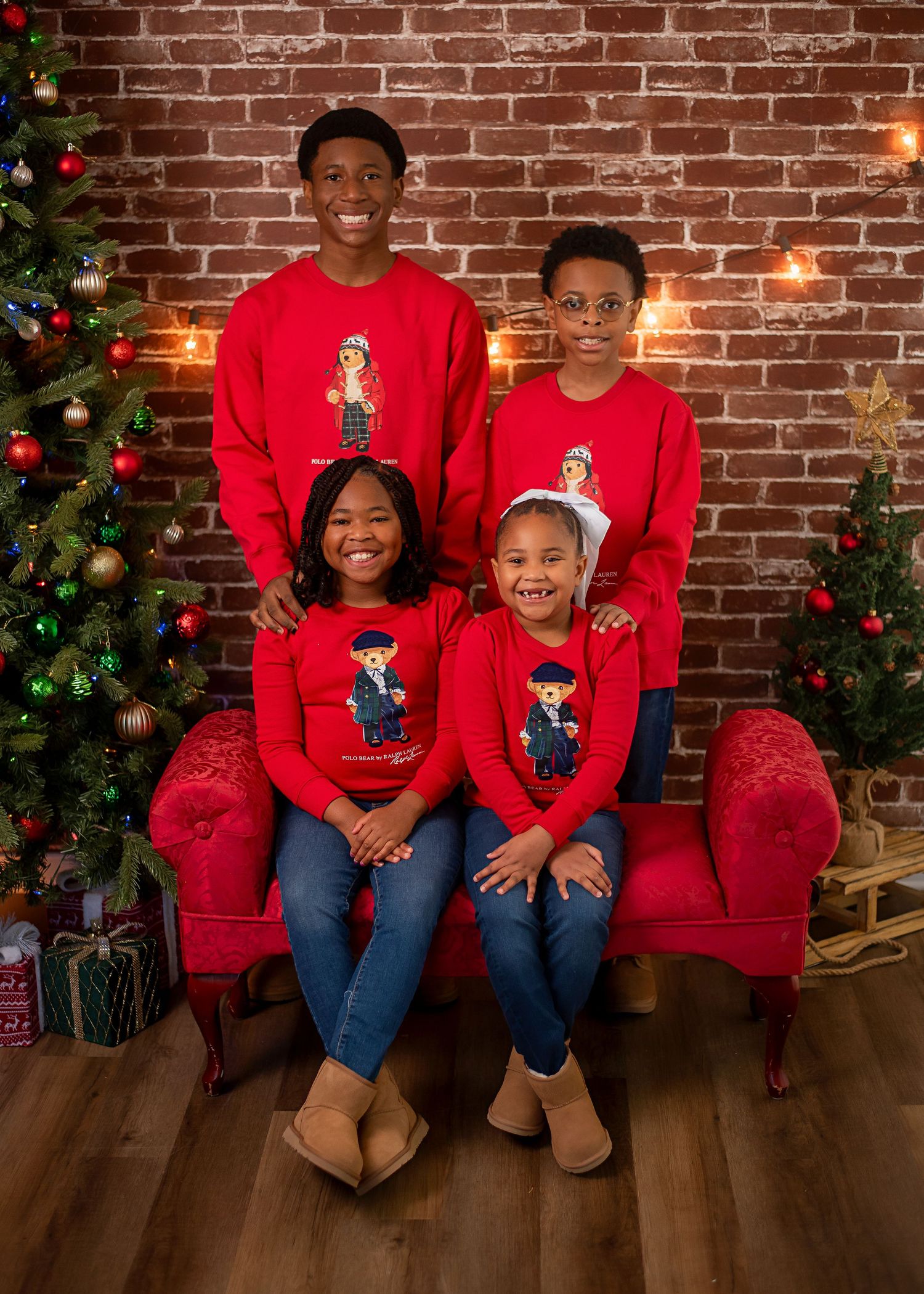 Family wearing matching red holiday sweaters posed in front of Christmas tree and brick wall.