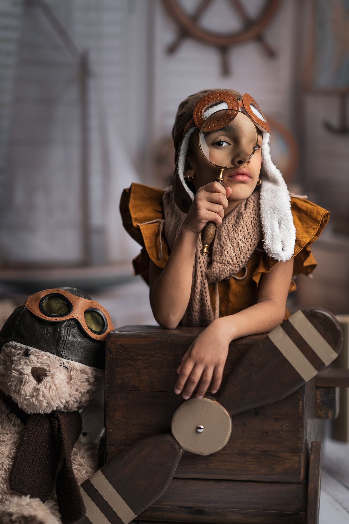 A dreamy vintage-inspired scene with aviator goggles, teddy bear, and wooden airplane prop in warm nostalgic lighting.