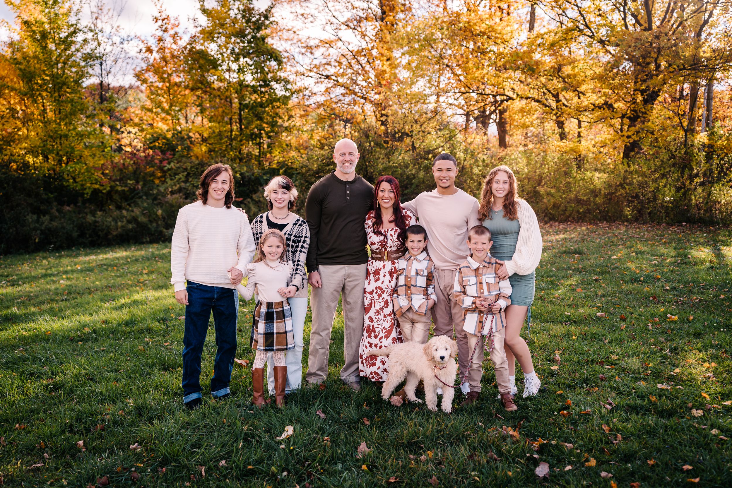A family with children and dogs poses for a group photo in an autumn setting.