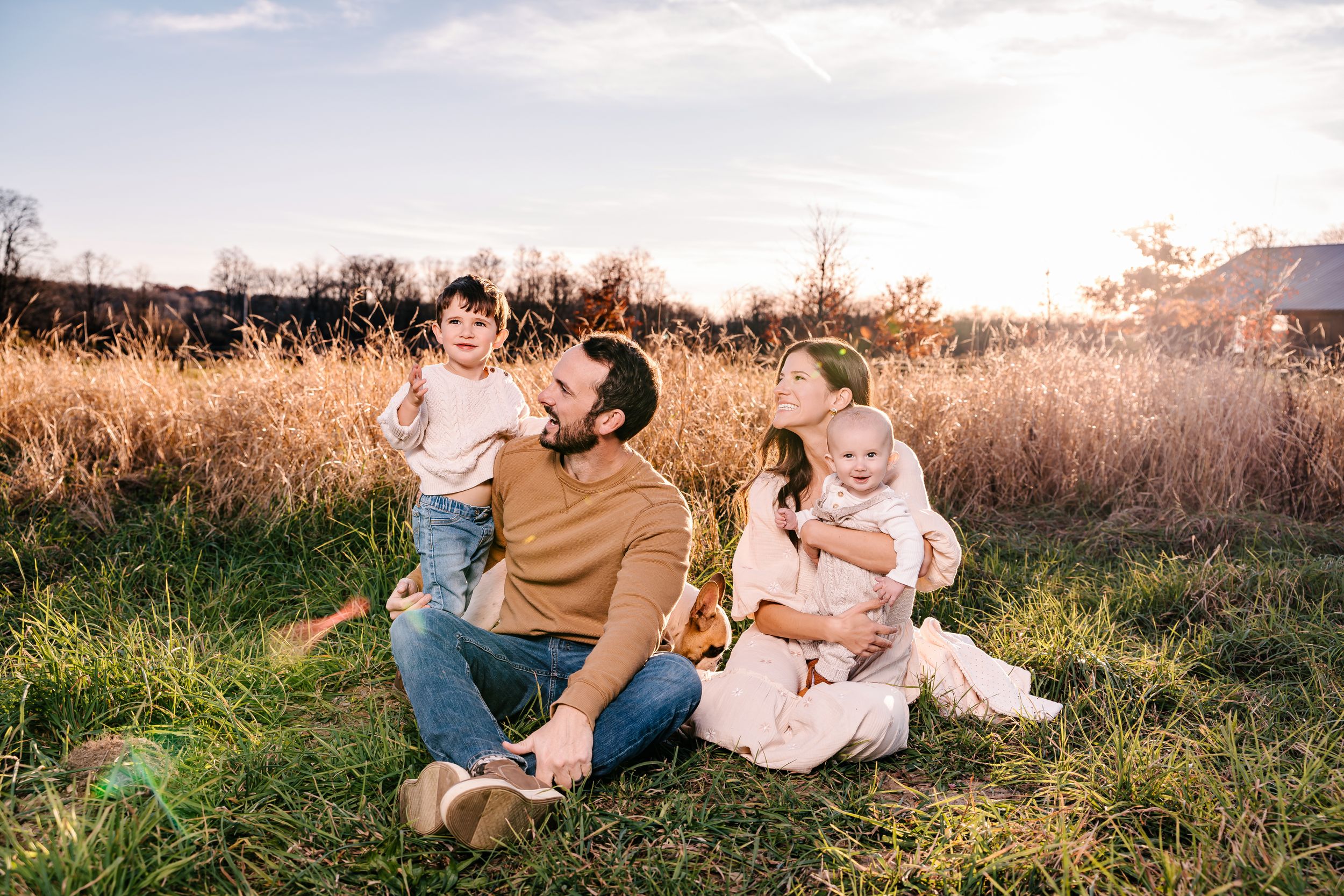 A family relaxes together in a sun-lit field of tall grass.