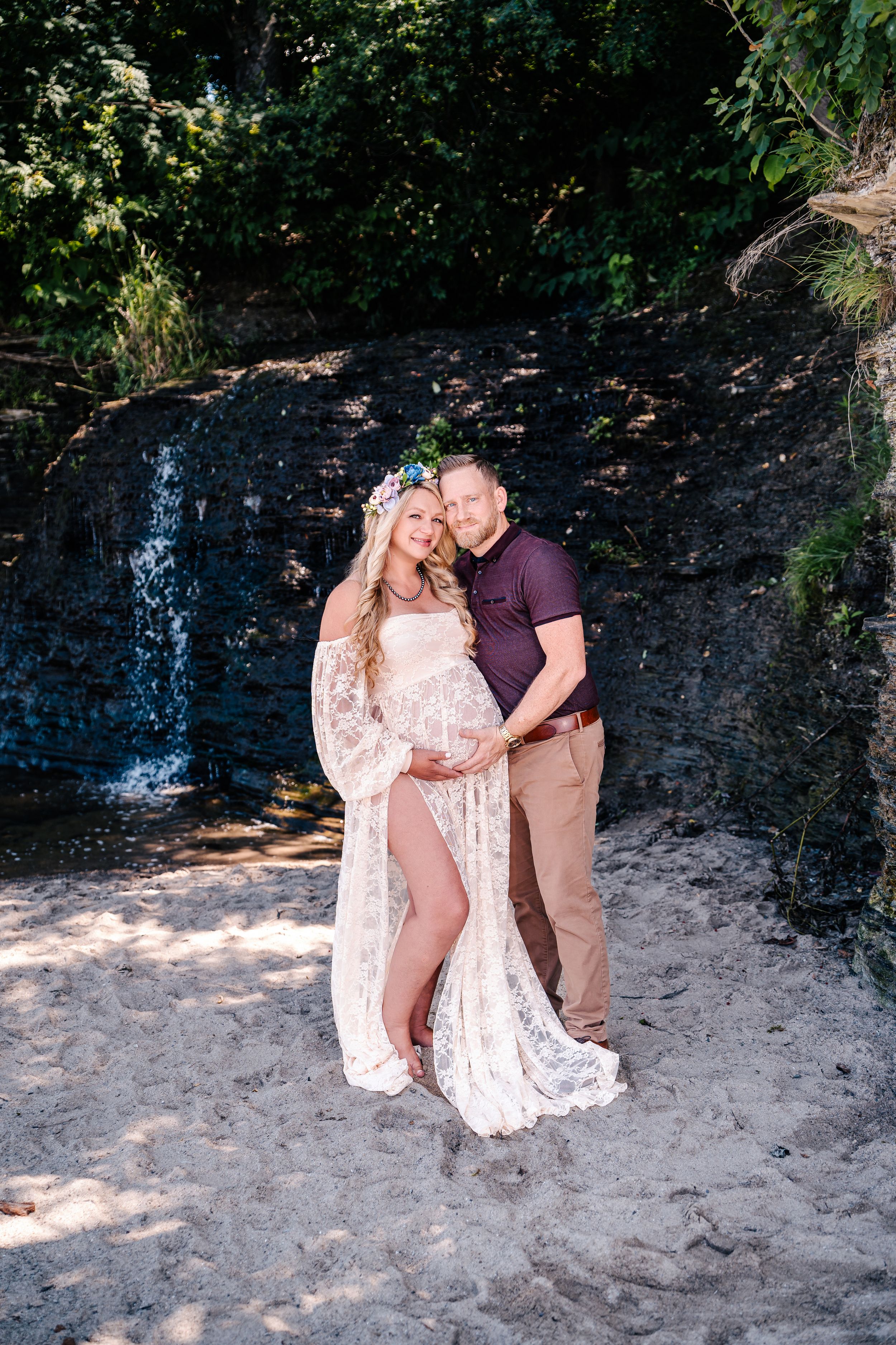 A maternity photoshoot featuring a couple posing by a scenic waterfall.