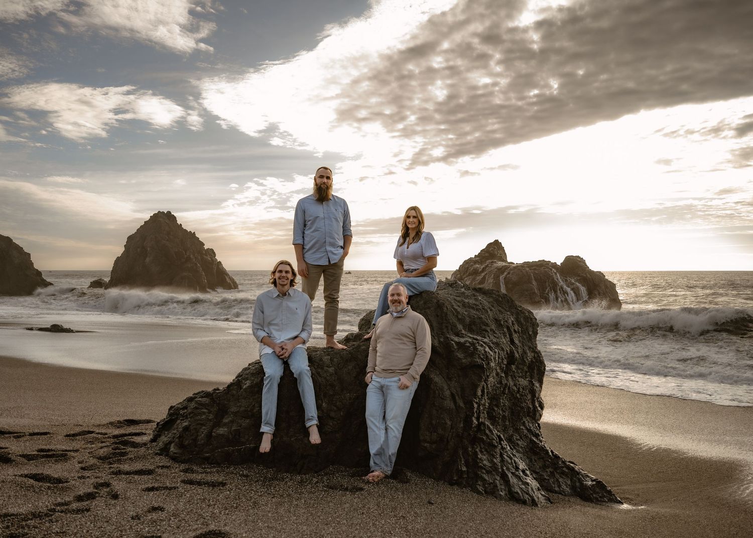 A group poses on coastal rocks at sunset with dramatic cloud formations overhead.