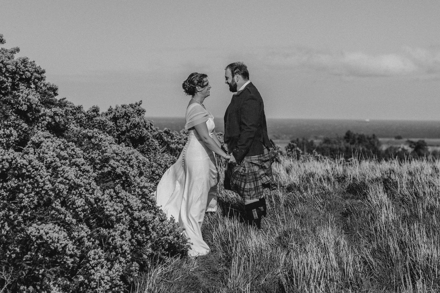 Black and white portrait of couple walking through Scottish coastal landscape.