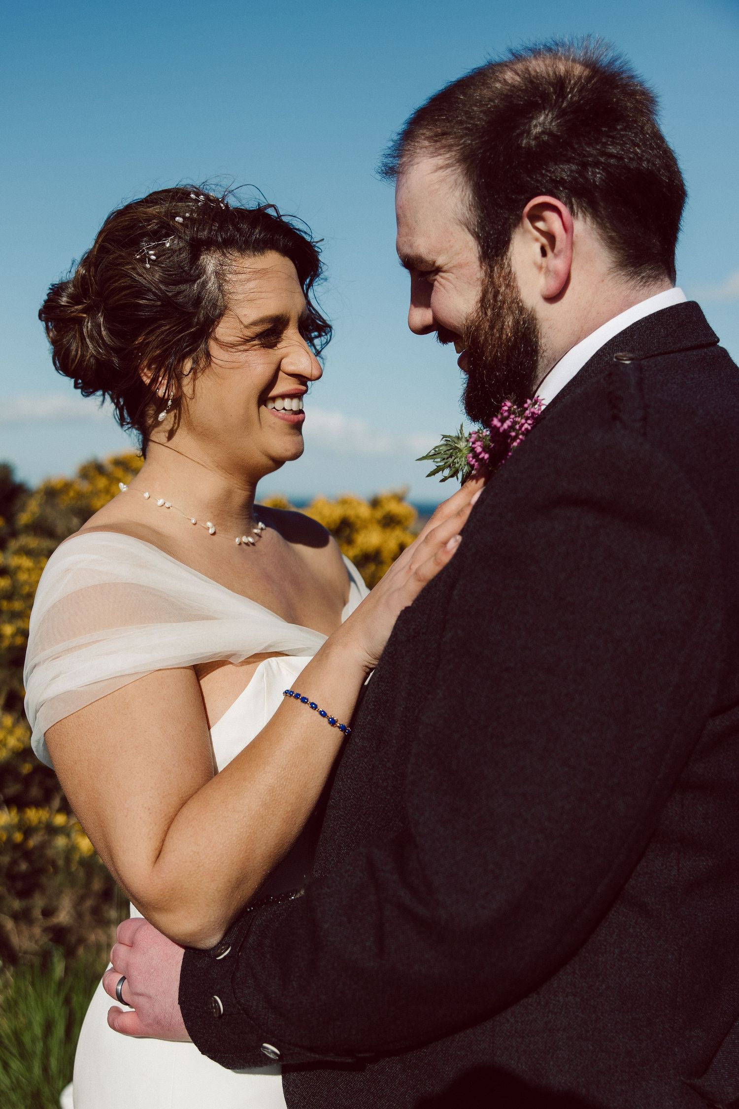 Close up of couple embracing outdoors with yellow gorse bushes in background.