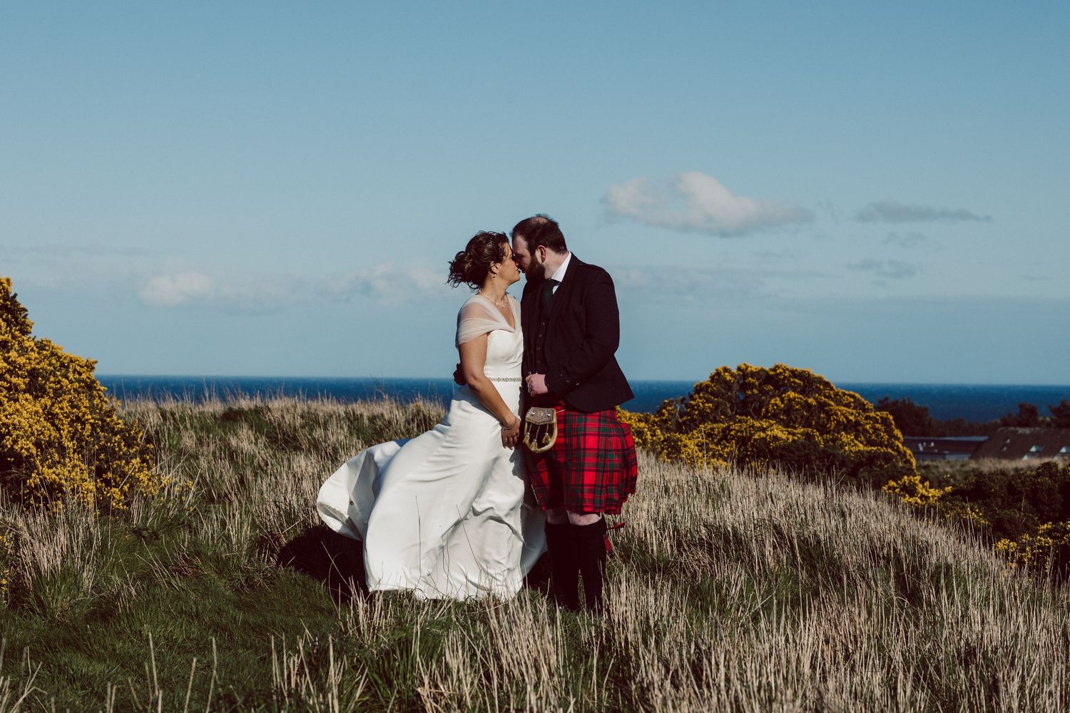 A romantic wedding portrait on a coastal hillside with ocean views and golden vegetation.