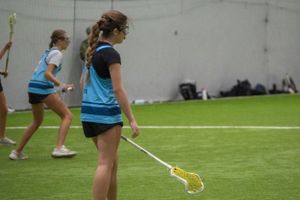 Players practice lacrosse drills on indoor turf field with yellow sticks.