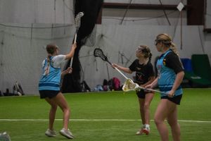 Three players participate in lacrosse drills during indoor practice.