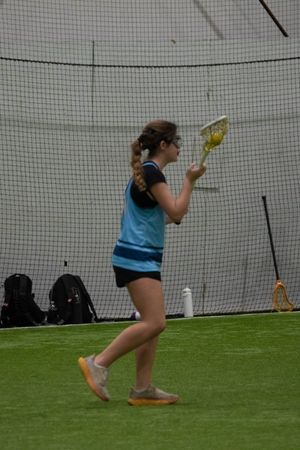 Player practices lacrosse stick handling technique on indoor turf field.