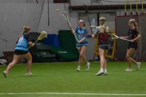 Athletes in blue and black uniforms compete for possession during an indoor lacrosse game.