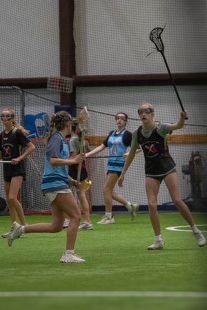 Players engage in a competitive indoor lacrosse match with raised sticks and focused positioning.