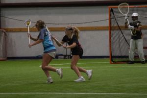 Two players battle for position near the lacrosse goal during an indoor match.