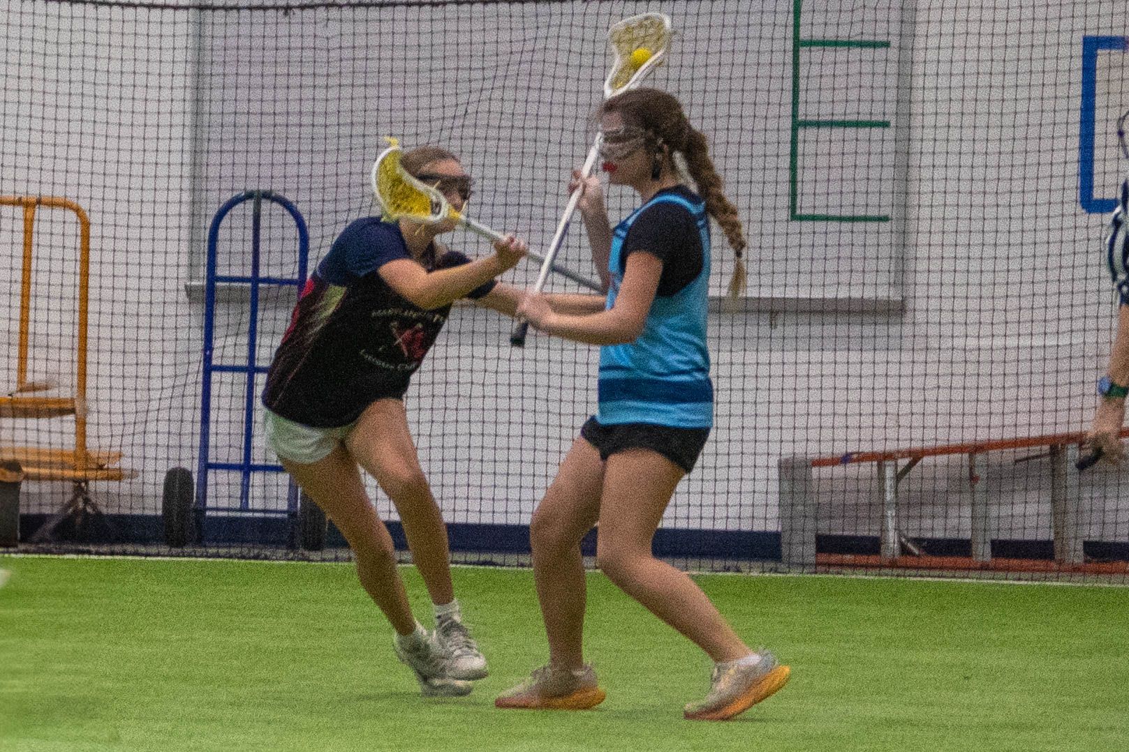 Female lacrosse players practicing drills on an indoor field.