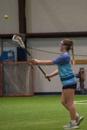 Player in blue jersey practicing catching drills with a lacrosse stick in an indoor facility.