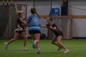 Athletic action shot of lacrosse players competing for ball control in an indoor arena.