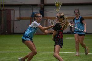 Two lacrosse players compete for the ball during an indoor practice match.