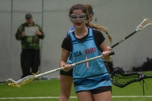 Player in protective eyewear holds lacrosse stick during indoor practice.
