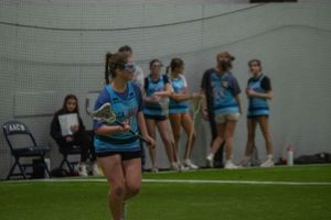 Indoor lacrosse practice session with players in light blue jerseys.