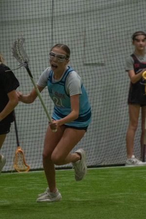 Player in protective gear carries lacrosse stick during indoor practice game.