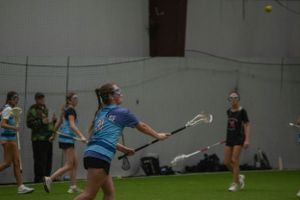 Lacrosse player with stick in motion on indoor turf field.