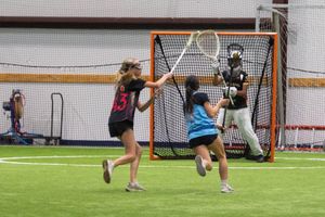 Lacrosse players practice shooting drills against a goalie in an indoor facility.