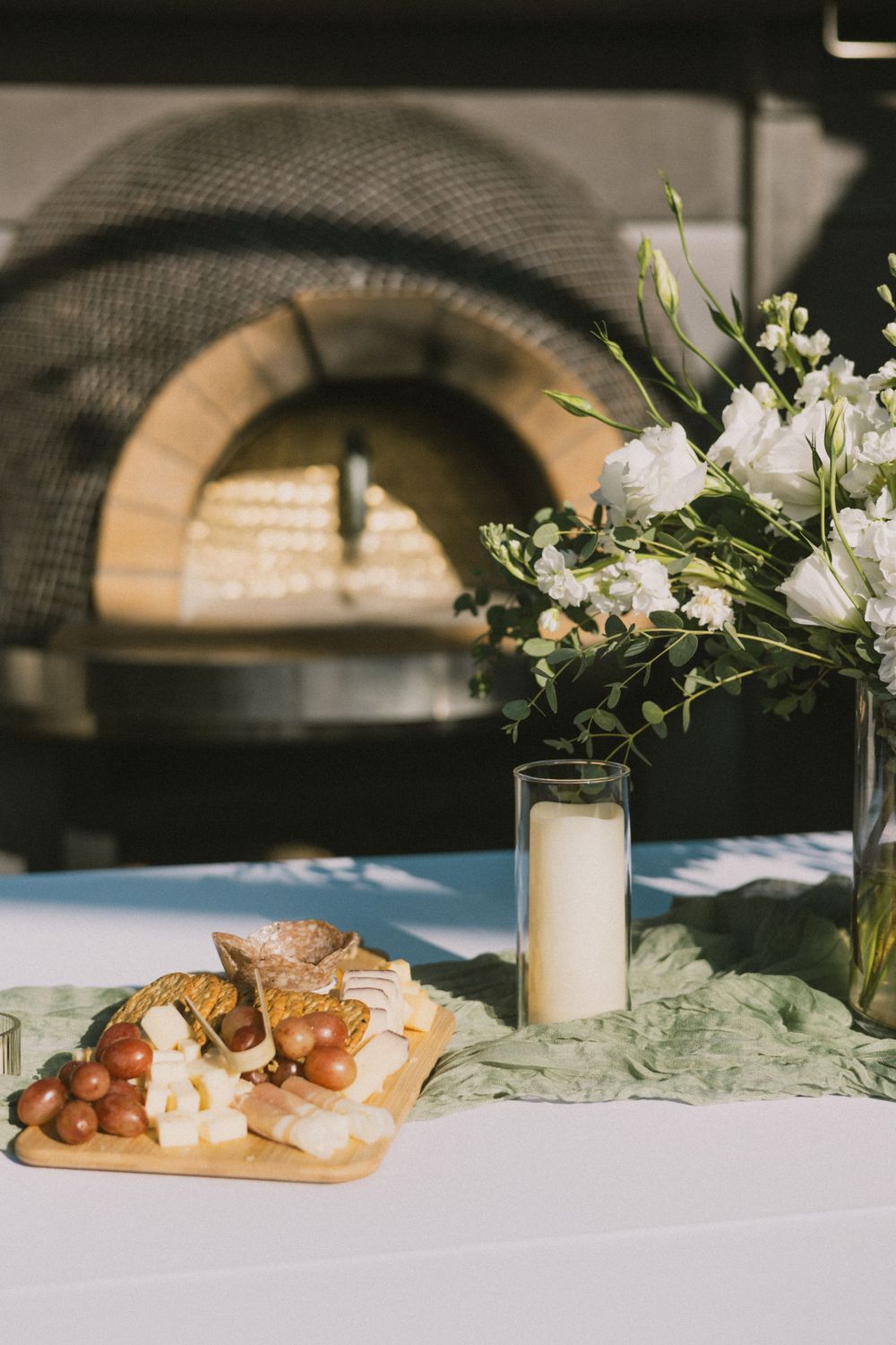 Charcuterie board and floral arrangement near brick pizza oven.