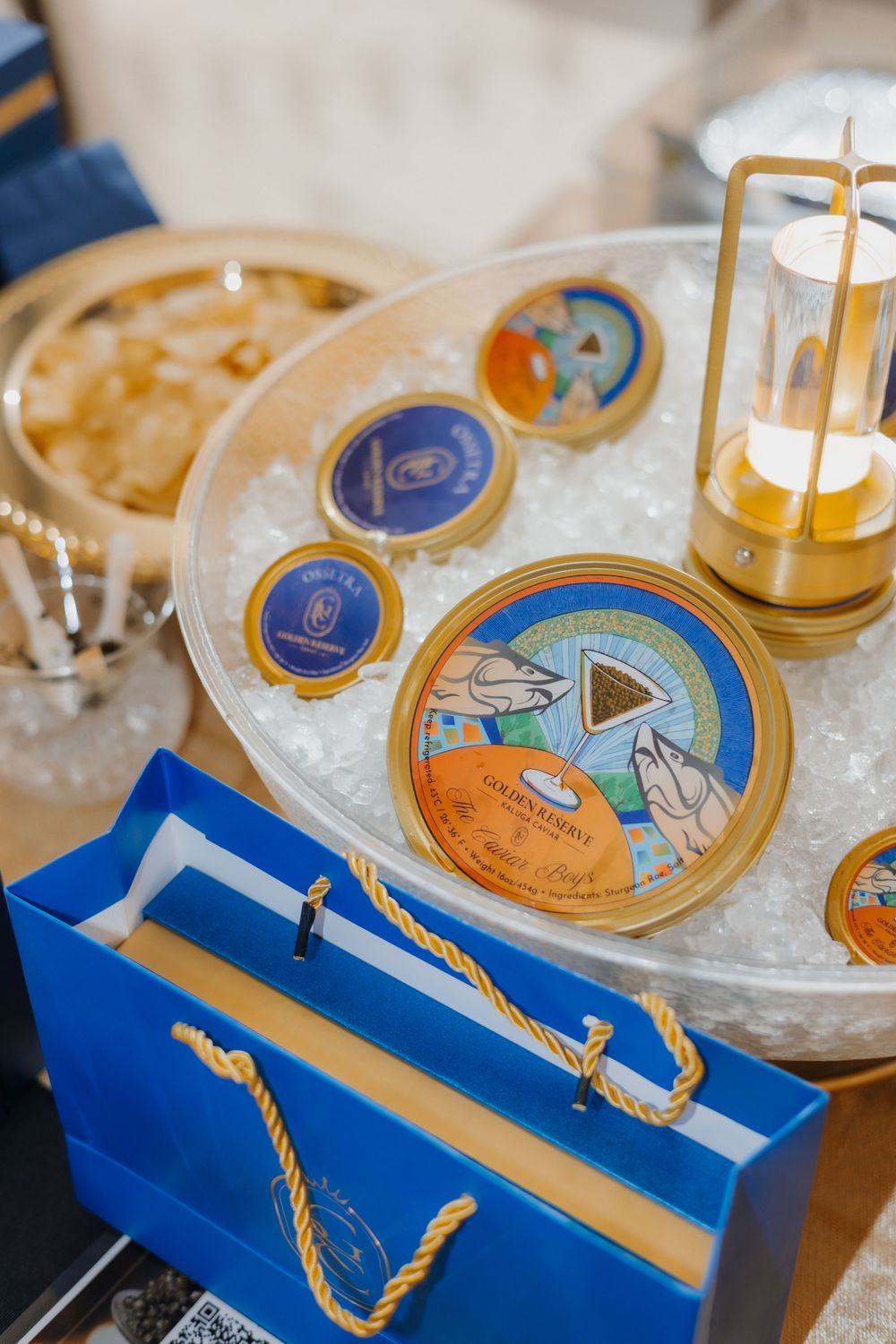 Luxury caviar tins displayed on ice with a blue gift bag and golden lantern at an elegant tasting event.