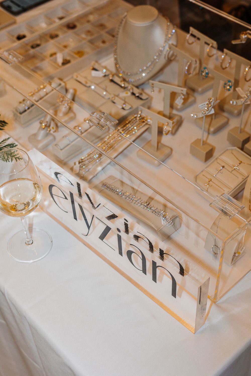 Elyzian jewelry display case with gold and silver pieces on white table at upscale event.
